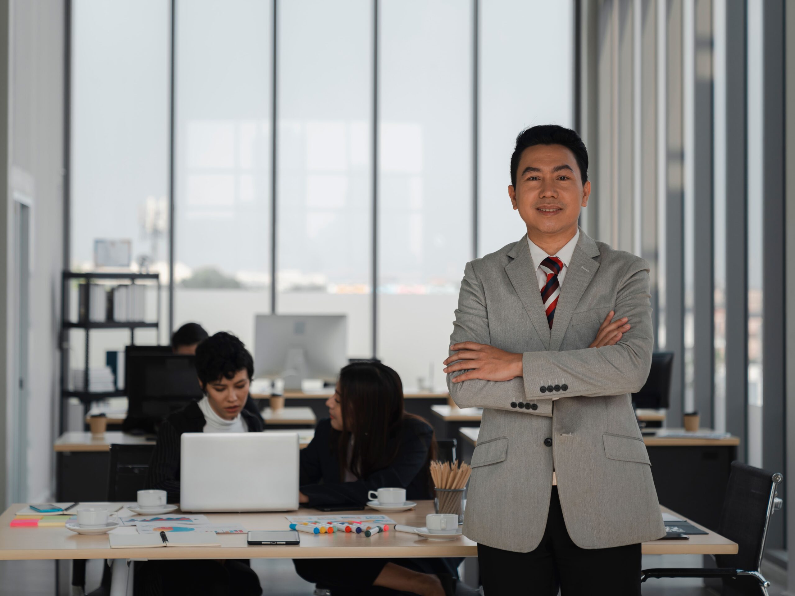 A corporate services director standing in a modern office with the team working behind